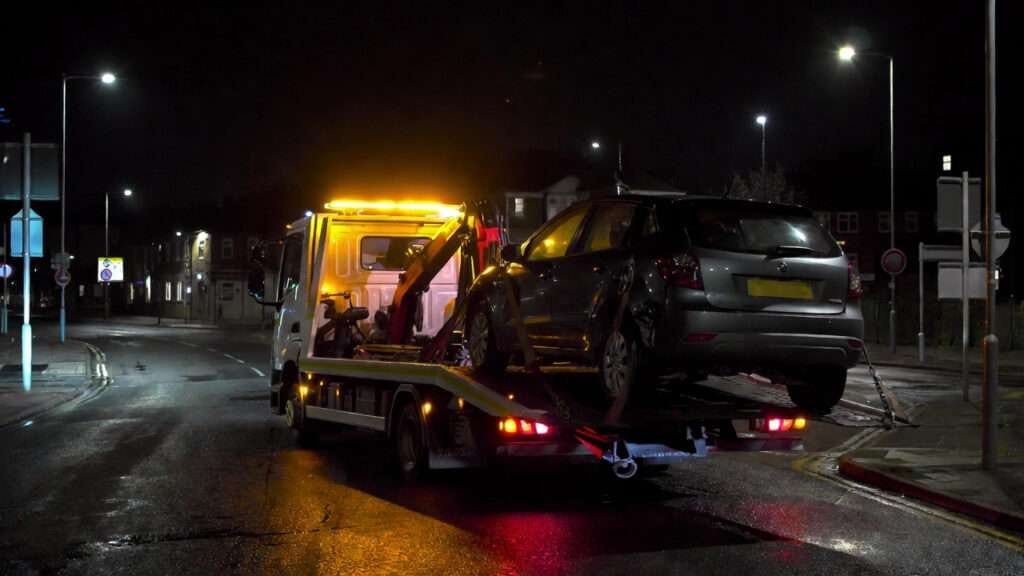 An NX Recovery flatbed truck attending a vehicle on a UK carriageway at dusk